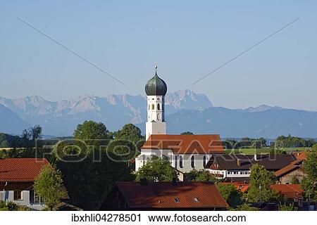 Stock Image - Pfarrkirche Maria Himmelfahrt, hinten Wettersteingebirge mit Zugspitze, Munsing am Starnberger See, Funfseenland, Oberbayern, Bayern, Deutschland, Europa. Fotosearch