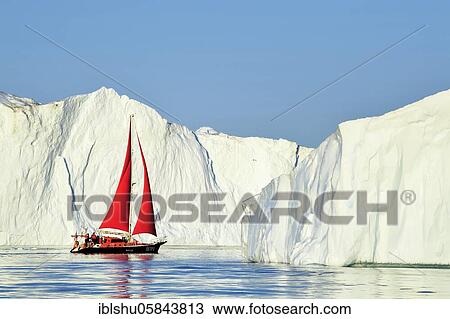 Stock Image - Red sailing boat in front of gigantic icebergs, Icefjord, UNESCO World Heritage Site, Disko Bay, Ilulissat, West Greenland, Greenland, North America. Fotosearch
