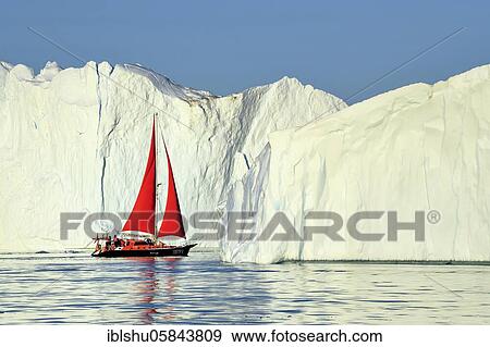 Stock Photo - Red sailing boat in front of gigantic icebergs, Icefjord, UNESCO World Heritage Site, Disko Bay, Ilulissat, West Greenland, Greenland, North America. Fotosearch