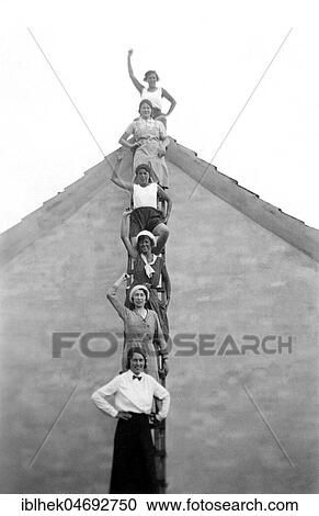 Stock Image - Six women standing on a ladder in front of a house waving, 1920s, Germany, Europe. Fotosearch