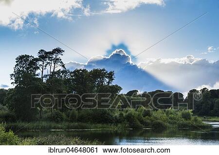 Stock Image - Sun breaking through the clouds, landscape at Dromoland Castle Hotel, County Clare, Republic of Ireland. Fotosearch