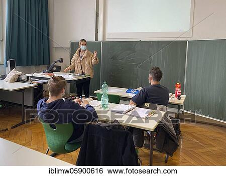 Stock Photograph - Teacher with thick winter jacket and face mask in classroom teaching, gestures, corona crisis, Stuttgart, Baden-Württemberg, Germany, Europe. Fotosearch