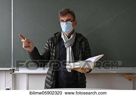 Stock Image - Teacher with thick winter jacket, scarf and face mask in classroom teaching, Corona crisis, Stuttgart, Baden-Württemberg, Germany, Europe. Fotosearch