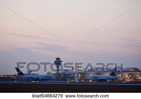 Stock Photo - Two Lufthansa Airbus aircrafts, A380-800, in front of Terminal 2 with tower, dusk, Munich Airport, Upper Bavaria, Bavaria, Germany, Europe. Fotosearch