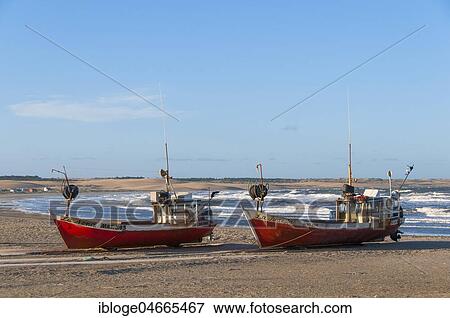 Stock Photo - Two red fishing boats lie on the beach of the Atlantic Ocean, village Cabo Polonio, Cabo Polonio National park, province Rocha, Uruguay, South America. Fotosearch