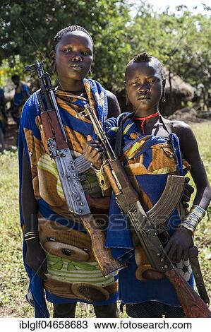 Stock Image - Two young women with Kalashnikovs, AK47, warrior, portrait, Mursi tribe, Southern Nations Nationalities and Peoples' Region, Ethiopia, Africa. Fotosearch