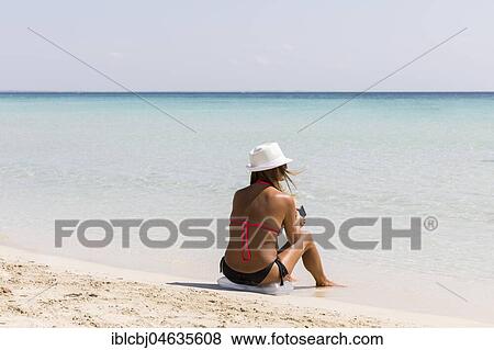 Stock Photo - Woman sitting down by the sandy beach, Puglia, Italy, Europe. Fotosearch