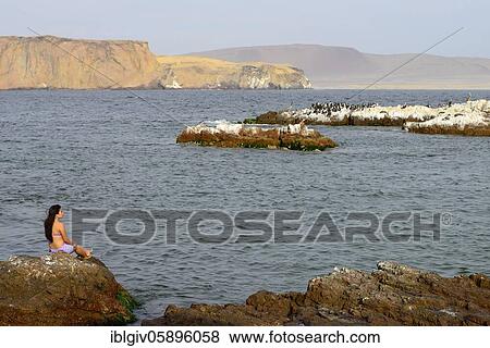 Stock Photo - Woman sitting on a rock in Paracas National Reserve, Paracas, Ica Region, Peru, South America. Fotosearch