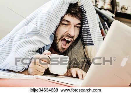 Stock Photo - Young man learns, yawns while working at the computer in bed, home office, Germany, Europe. Fotosearch