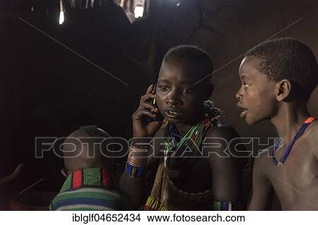 Picture - Young woman with children, mobile phone calls in the mud hut, Hamer tribe, Turmi, Region of the Southern Nations, Ethiopia, Africa. Fotosearch