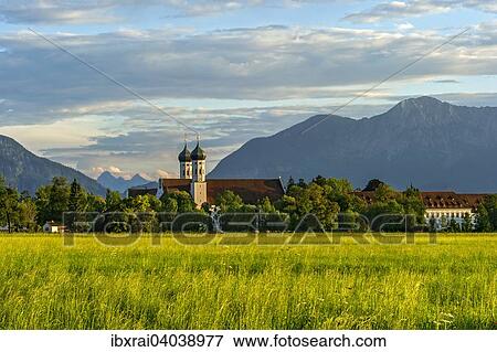 Stock Photo - Basilika St. Benedikt, Benediktinerabtei Kloster Benediktbeuern, hinten links Jochberg, rechts Herzogstand und Heimgarten der Voralpen, ganz hinten Arnspitzgruppe im Wettersteingebirge der Alpen, Benediktbeuern, Oberbayern, Bayern, Deutschland, Europa. Fotosearch