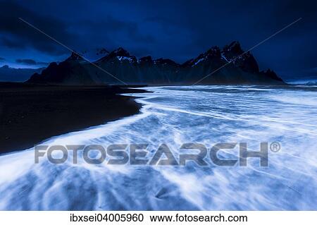 Stock Image - Berggipfel mit Meeresbrandung zur blauen Stunde, Hofn, Island, Europa. Fotosearch
