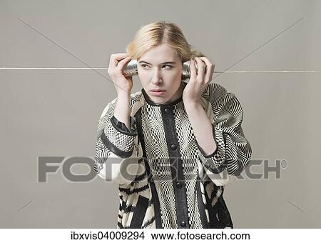 Picture - Blonde Frau hort an einem Dosentelefon, Konzept, Spionage, Uberwachung und Kommunikation. Fotosearch