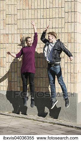 Ein junger Mann und eine Frau springen in die Luft und klatschen sich dabei ab, Schweden, Europa View Large Photo Image Stock Photography - Ein junger Mann und eine Frau springen in die Luft und klatschen sich dabei ab, Schweden, Europa. Fotosearch