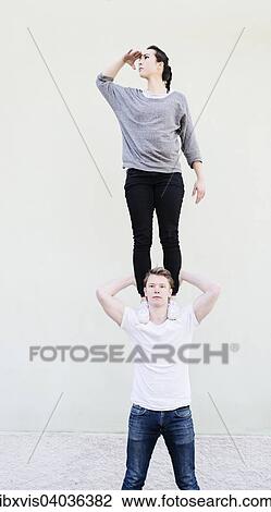 Stock Image - Eine Frau steht auf der Schulter eines Mannes und blickt in die Ferne, suchend, Symbolbild, Teamarbeit, Unterstutzung und Weitsicht. Fotosearch