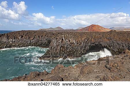 Stock Photography - Felskuste von Los Hervideros, Vulkanlandschaft, hinten Feuerberge im Timanfaya Nationalpark, Lanzarote, Kanarische Inseln, Spanien, Europa. Fotosearch