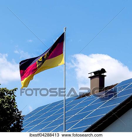 Stock Image - Hausdach mit Solarzellen, davor eine Deutschlandfahne, Energiewende in Deutschland. Fotosearch