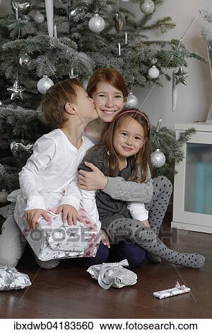 Stock Image - Heiligabend, Geschwister freuen sich uber Weihnachtsgeschenke unter dem Weihnachtsbaum, Bayern, Deutschland, Europa. Fotosearch