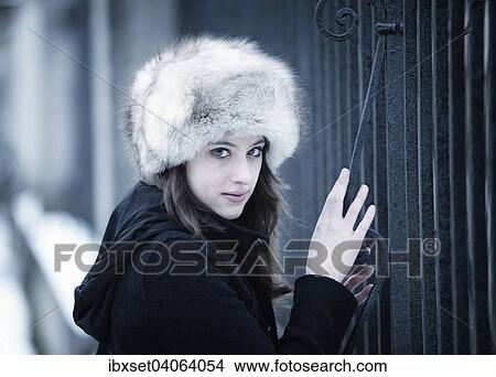Picture - Junge Frau mit Pelzmutze im Winter an einem Gittertor. Fotosearch