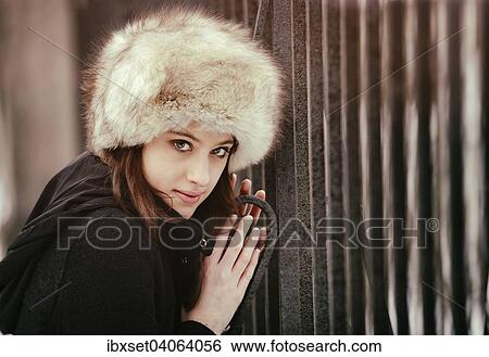 Stock Photograph - Junge Frau mit Pelzmutze im Winter an einem Gittertor. Fotosearch