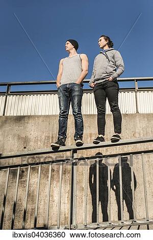 Stock Image - Lassig und entspannter junger Mann und eine junge Frau stehen auf einem Gelander in einem Stadtgebiet, Schweden, Europa. Fotosearch
