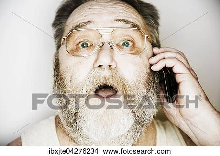 Senior mit Vollbart und Brille im Unterhemd telefoniert mit einem Smartphone, Portrait, Deutschland, Europa View Large Photo Image Picture - Senior mit Vollbart und Brille im Unterhemd telefoniert mit einem Smartphone, Portrait, Deutschland, Europa. Fotosearch