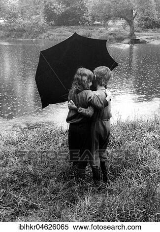 Stock Photography - 2 children kiss each other under the umbrella ca. 1970s, exact place unknown, Czech Republic, Europe. Fotosearch