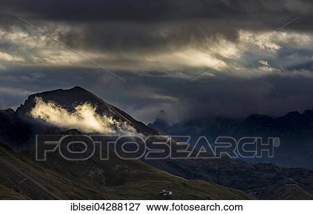 Stock Photo - Clouds with sunny spot in front of dark mountain peaks, Allgau Alps, Warth, Vorarlberg, Austria, Europe. Fotosearch