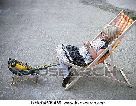 Stock Photography - Girl with parrot in deck chair, England, Great Britain. Fotosearch