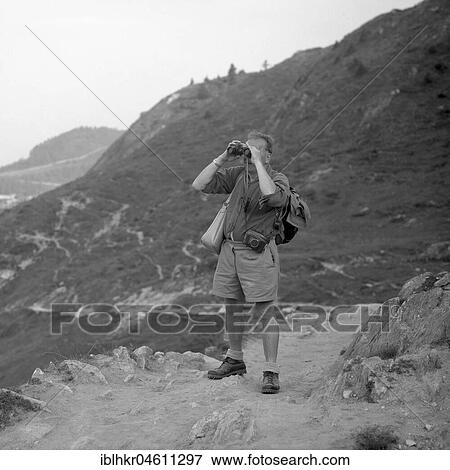 Man standing on a mountain path looking through binoculars, ca. 1950, near Freiburg, Germany, Europe View Large Photo Image Stock Photo - Man standing on a mountain path looking through binoculars, ca. 1950, near Freiburg, Germany, Europe. Fotosearch