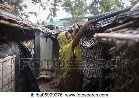 Stock Photograph - Rohingya woman covers the roof of her hut with a carpet to keep the interior dry during the heavy monsoon rains, Camp Kutupalong, Cox Bazaar, Bangladesh, Asia. Fotosearch