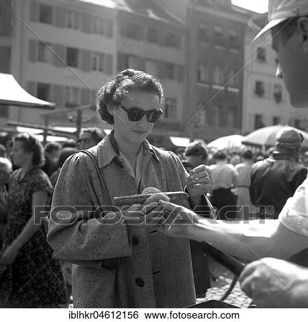 Stock Photograph - Seller hands a woman a sausage in bread, Freiburg ca. 1945 to 1955. Fotosearch