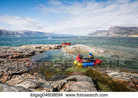 Two persons with packing trucks on fjord, rocks, behind mountains, Greenland, North America View Large Photo Image Picture - Two persons with packing trucks on fjord, rocks, behind mountains, Greenland, North America. Fotosearch
