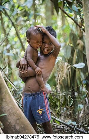 Stock Photograph - Young boy, aboriginal Orang Asil, holding his crying baby brother in his arms, indigenous culture, tropical rainforest, Taman Negara, Malaysia, Asia. Fotosearch
