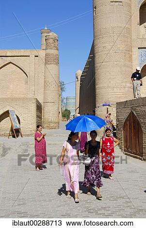 Stock Image - Colourful dressed women with umbrella in an alley Khiva Uzbekistan. Fotosearch