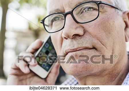 Stock Image - Grey-haired senior with glasses talking on the phone with his smartphone, Germany, Europe. Fotosearch