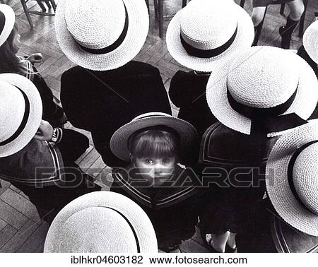 Stock Image - Little child looks up, standing between kids wearing straw hats, England, Great Britain. Fotosearch