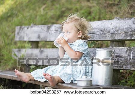 Stock Photo - Madchen trinkt Milch auf einer Bank vor der Alm, Deutschland, Europa. Fotosearch