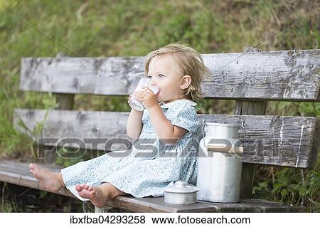 Stock Photo - Madchen trinkt Milch auf einer Bank vor der Alm, Deutschland, Europa. Fotosearch