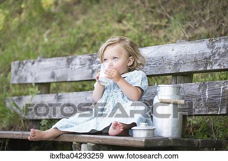 Stock Photo - Madchen trinkt Milch auf einer Bank vor der Alm, Deutschland, Europa. Fotosearch