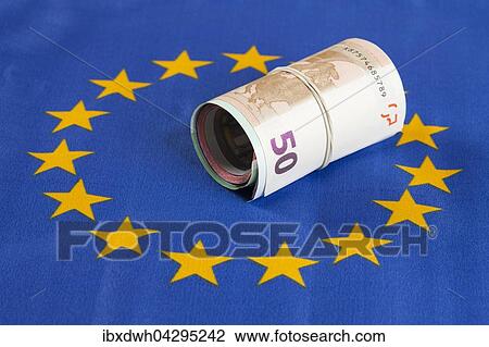 Stock Image - Rolle mit Gummiband, mehrere Geldscheine, Euro-Scheine liegen auf Europa-Fahne. Fotosearch