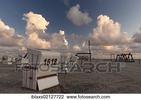 Stock Image - Roofed wicker beach chairs on the beach of Sankt Peter-Ording at sunset, North Friesland district, Schleswig-Holstein, Germany, Europe. Fotosearch
