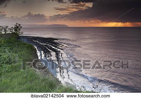 Picture - Setting sun shining through a heavy cloud with rays over the Bristol Channel, from the cliffs above Kilve Beach, Somerset, England, United Kingdom, Europe. Fotosearch