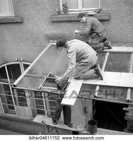 Stock Image - Three roofers repair a canopy with glass panels, around 1950, Freiburg, Germany, Europe. Fotosearch