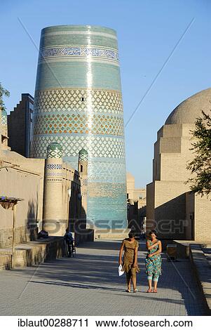 Stock Image - Two women in the alley with unfinished Kalta Minor minaret in the background Khiva Uzbekistan. Fotosearch