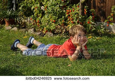 Stock Photography - Boy lying on grass, resting head in hands, looking thoughtful. Fotosearch