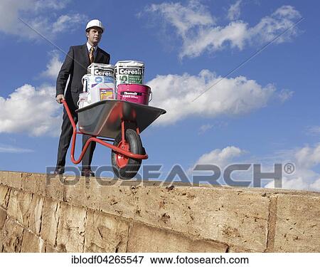 Man wearing a suit and helmet pushing a wheelbarrow with building materials along a wall, Germany, Europe View Large Photo Image Stock Photo - Man wearing a suit and helmet pushing a wheelbarrow with building materials along a wall, Germany, Europe. Fotosearch