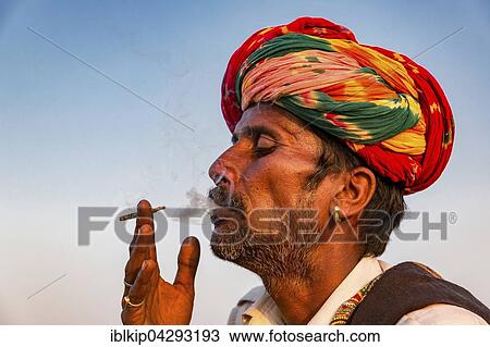 Stock Image - Portrait of Rajasthani man with turban smoking a cigarette, Pushkar, Rajasthan, India, Asia. Fotosearch