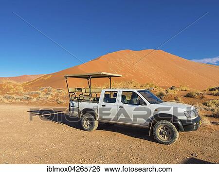 Stock Photograph - Terrain vehicle in front of a sand dune of the Namib Desert, Hardap Region, Namibia, Africa. Fotosearch