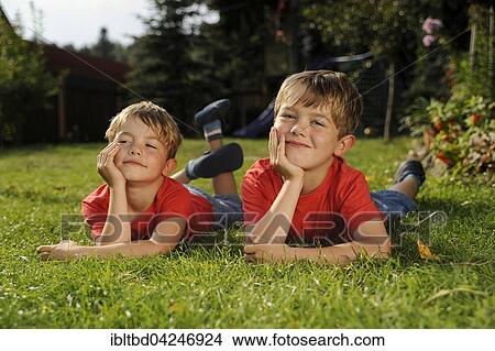 Twins lying on grass in garden, resting head on hands View Large Photo Image Picture - Twins lying on grass in garden, resting head on hands. Fotosearch